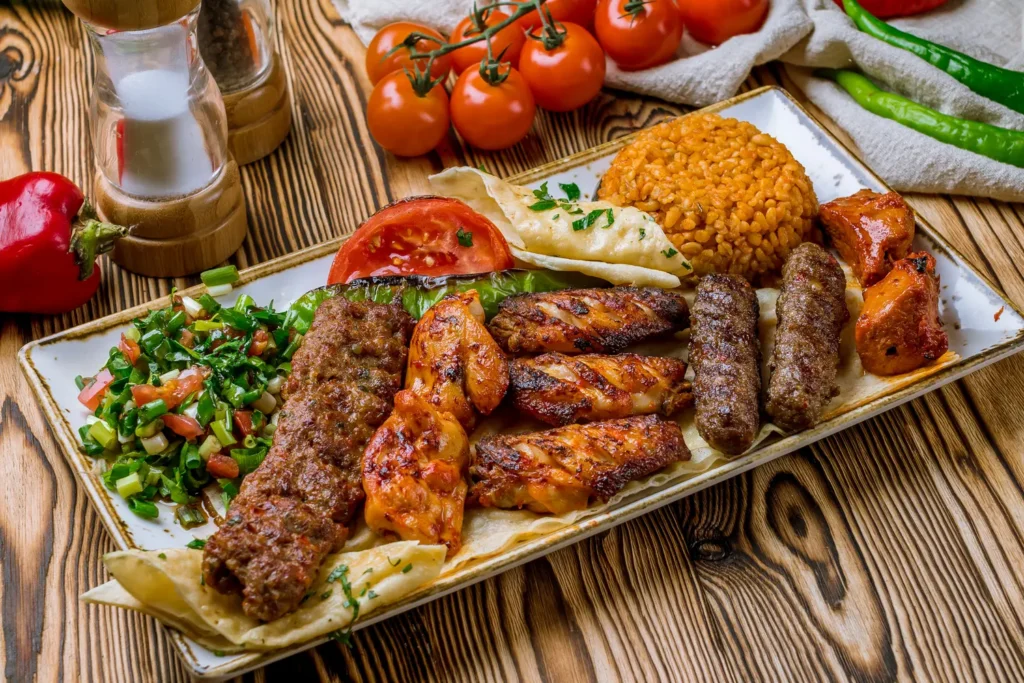 Ein rechteckiger Teller mit Grillspießen, Salat, Tomaten, Reis und gegrilltem Gemüse